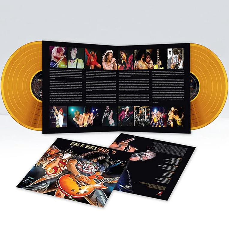 Exploded view of 'Guns N' Roses Brazil '91' vinyl record set. The set includes two bright orange vinyl records and an open gatefold with multiple live concert photos of the band members and detailed text about the performance. The additional inserts feature more concert imagery and track listings. The cover art showcases a dynamic image of the band performing live, with Slash prominently playing his guitar.