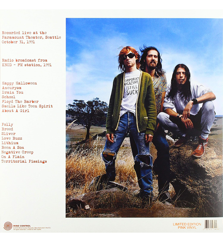 Vinyl record back cover for 'Nirvana Happy Halloween.' The cover features a full-length photo of the three band members, Kurt Cobain, Krist Novoselic, and Dave Grohl, standing in an outdoor setting with a clear blue sky. The left side of the cover lists the track titles recorded live at the Paramount Theatre in Seattle on October 31, 1991. The text also mentions the radio broadcast from KNDD - FM station, 1991. Marked as a limited edition.