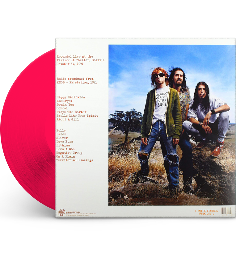 Vinyl record back cover for 'Nirvana Happy Halloween.' The cover features a full-length photo of the three band members, Kurt Cobain, Krist Novoselic, and Dave Grohl, standing in an outdoor setting with a clear blue sky. The left side of the cover lists the track titles recorded live at the Paramount Theatre in Seattle on October 31, 1991. The text also mentions the radio broadcast from KNDD - FM station, 1991. The vinyl itself is a vibrant pink colour, marked as a limited edition.