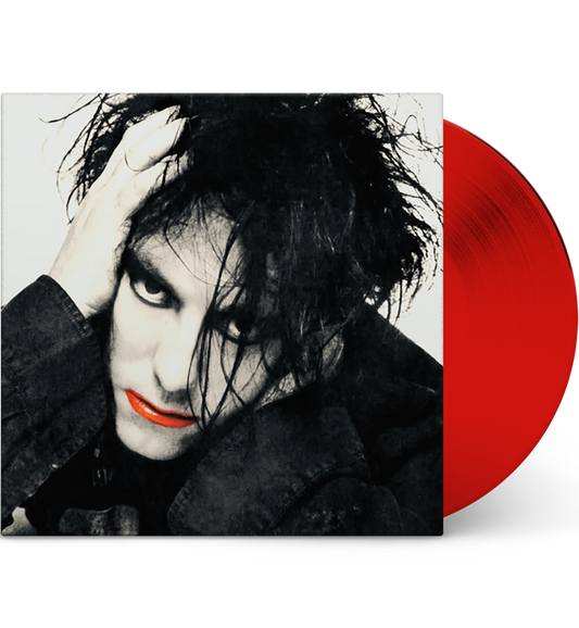 A mockup image of a vinyl record ‘The Cure – Live in Washington, D.C., 1984’. The cover displays a high-contrast black and white portrait of Robert Smith with wild, dark hair and heavy eyeliner. His face partially covered by his hand, which rests on his head. His lips are painted bright red, adding a splash of color to the monochromatic image. The vinyl record is bright red, partially visible on the right side of the image.